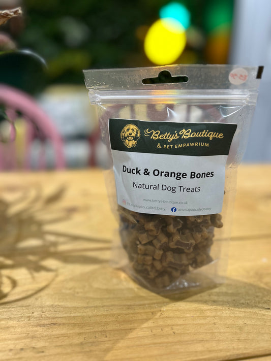 Pack of duck and orange bones natural dog treats from Betty's Boutique on a wooden surface.