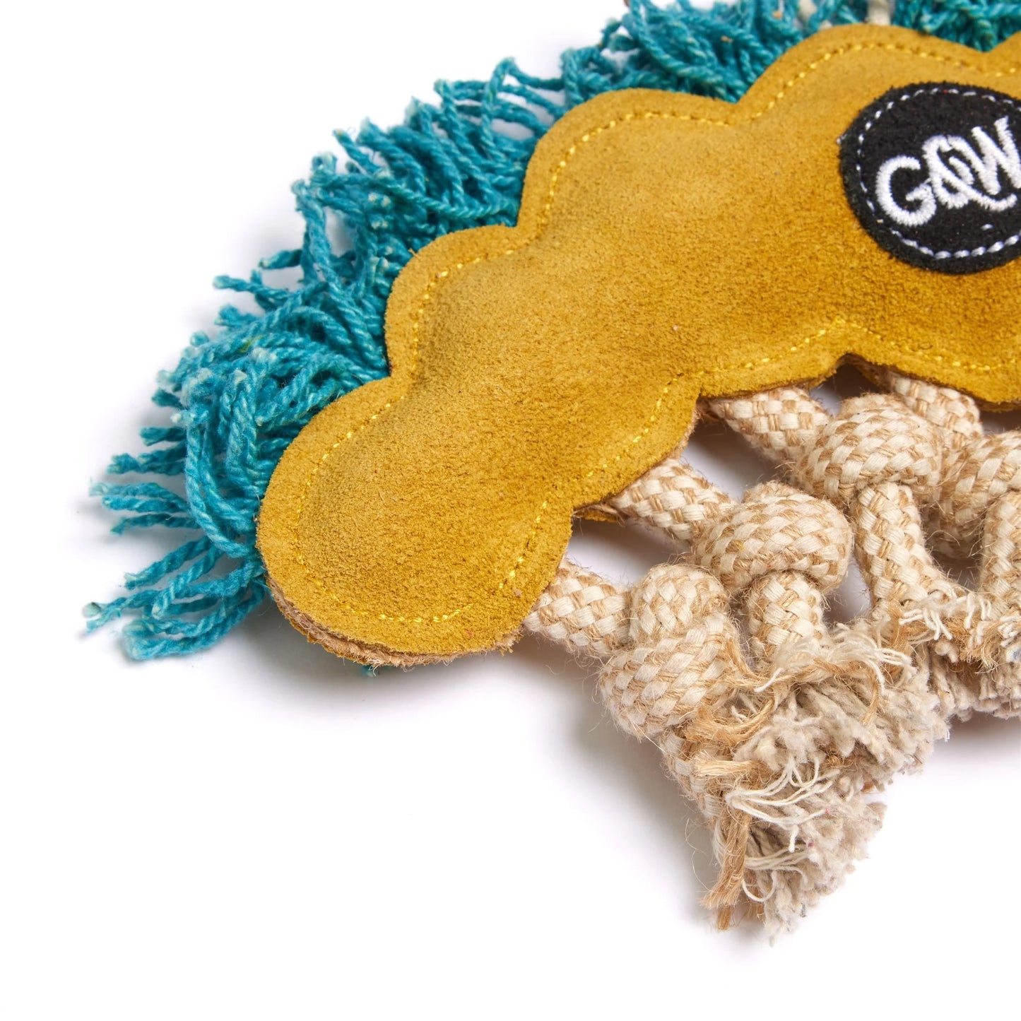Close-up of a dog chew toy featuring a mustard yellow suede cloud-shaped pad, turquoise blue yarn fringes, and a beige braided rope, with a black circular patch showing the brand 'G&W'.