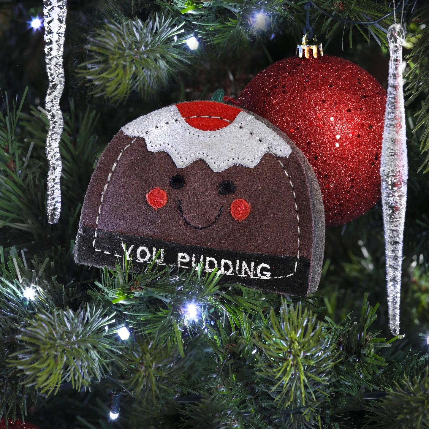 Christmas dog toy shaped like a pudding with a face, hanging on a decorated tree.